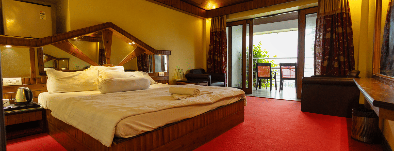 A bedroom with a king size bed, seating area, red carpet, and open balcony door at Hotel Seagull Digha.